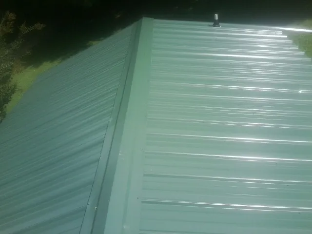 New green metal panels meeting at the ridge of a roof — Flat Roof Repair work by our crew in Butler